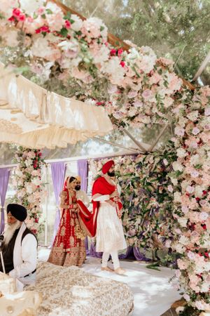Wedding ceremony under floral-decorated tent with pink and white blooms.