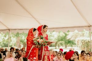 Traditional Sikh wedding ceremony with red attire and floral arrangements under outdoor tent.