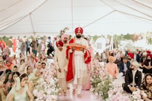 Traditional Sikh ceremony procession in a tent with a decorated aisle lined with pink and white flowers.