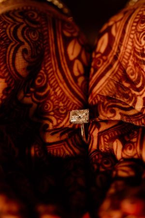 Close-up of an engagement ring against intricate henna designs in warm lighting.