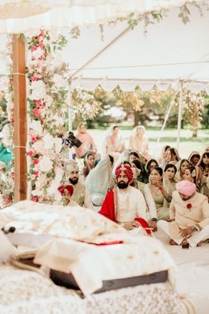 Wedding ceremony guests seated under a tent decorated with floral garlands and hanging blooms.