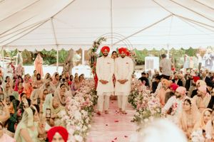 Traditional Indian wedding ceremony setup under white tent with floral decorations and seated guests.