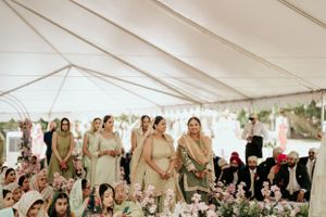 Wedding guests gathered under white tent with elegant pastel decor and floral arrangements.