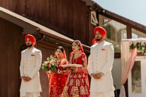 Wedding party in traditional Sikh attire standing against wooden building backdrop.