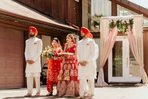 Traditional Sikh wedding party poses outside venue with white and pink decor elements.