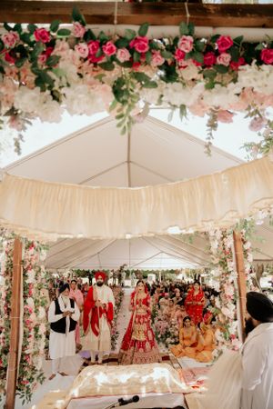 White tent decorated with pink roses and greenery for traditional Indian wedding ceremony.