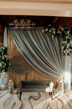 An elegant wedding backdrop with draped gray fabric, floral arrangements, and vintage furniture.