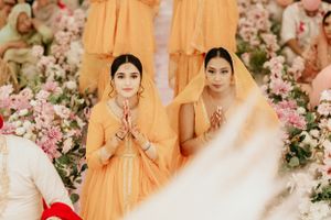 Attendants in orange dresses stand amid pink floral decorations at a traditional wedding ceremony.