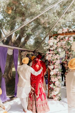 Traditional Indian wedding ceremony under a white tent with vibrant red bridal attire and floral decorations.