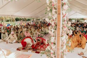 Large gathering of wedding guests seated under decorated tent during traditional ceremony.