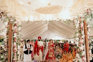 Wedding ceremony procession under decorated tent with floral arrangements and draped fabric.