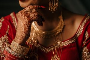 Intricate henna designs and gold bangles on hands wearing traditional Indian bridal attire.