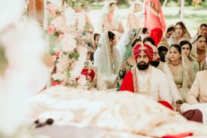 Guests observe a traditional Sikh wedding ceremony under a tent with floral decorations.
