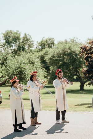 Three musicians in matching white uniforms playing trumpets outdoors during an event.