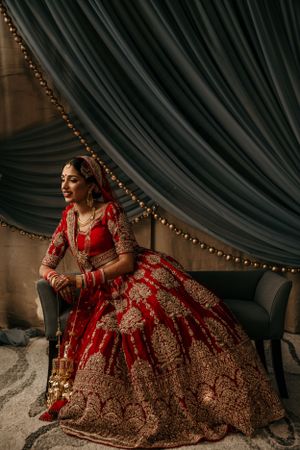 Elegant red and gold traditional Indian bridal lehenga displayed in luxurious setting with draped curtains.