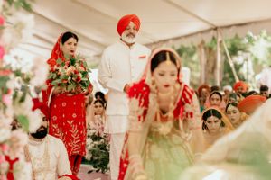 Wedding ceremony under white tent with traditional red and white attire and floral decorations.