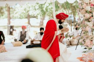 Person in traditional red Sikh attire participating in wedding rituals under a decorated tent.