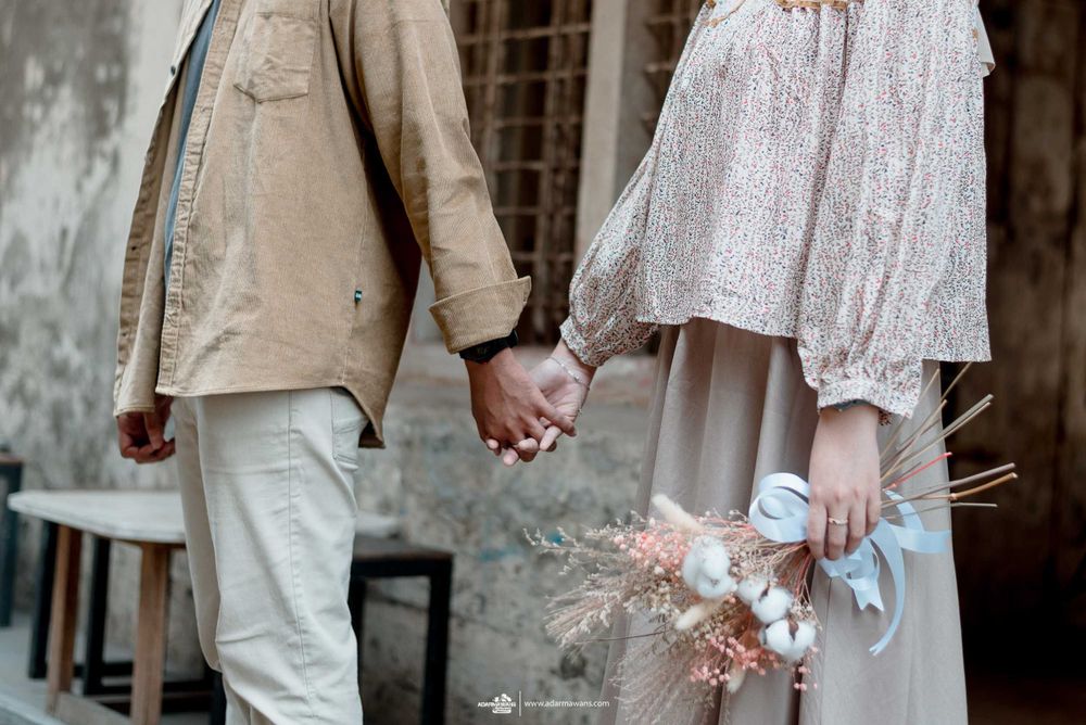 Close-up of couple holding hands with dried flowers against vintage wall background.