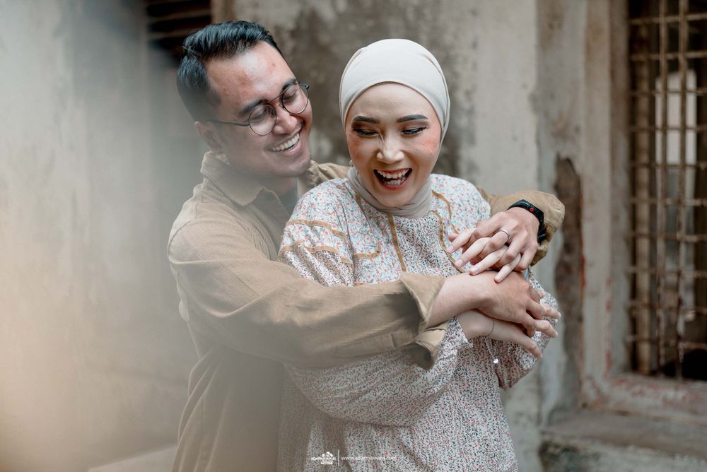 Couple sharing joyful moment while embracing against weathered wall.