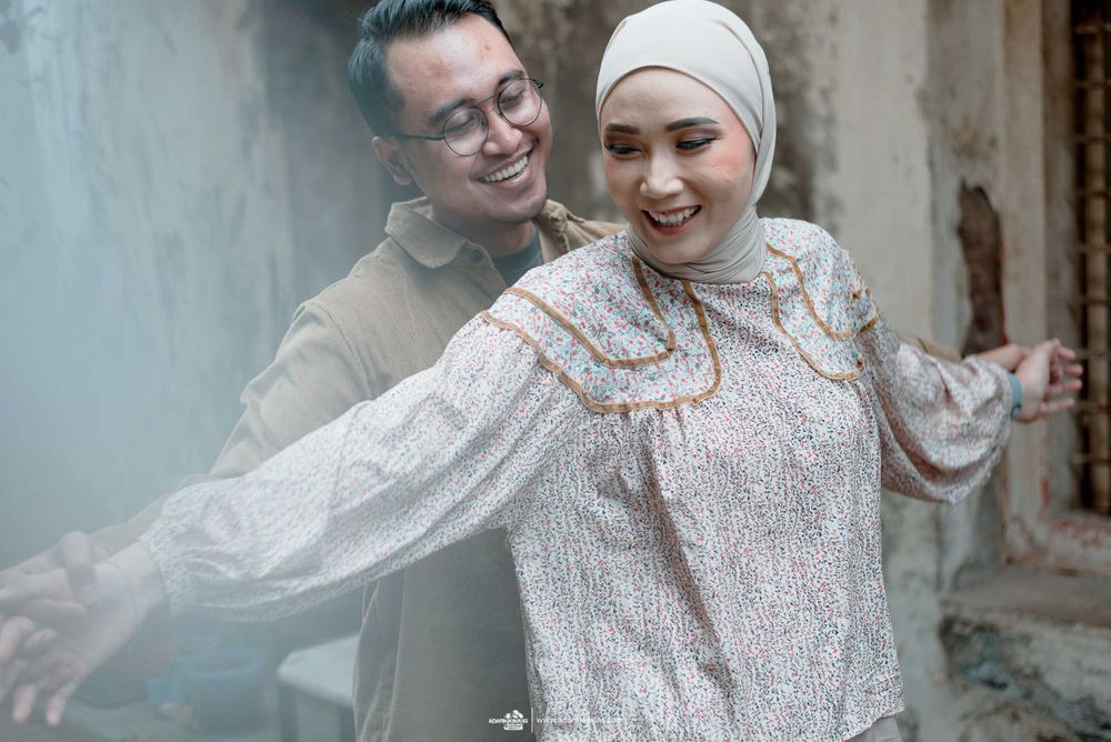 Couple embracing in romantic photoshoot against rustic wall background.