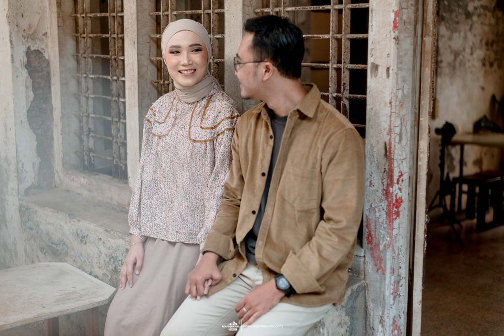 Couple in coordinated neutral outfits pose against textured wall during photoshoot.