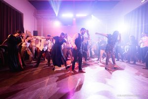 Purple-lit dance floor filled with party guests dancing at an indoor celebration.
