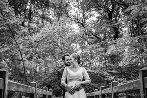 Black and white outdoor garden wedding ceremony with guests seated among lush trees and greenery.