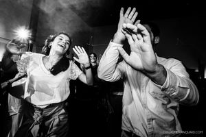 Black and white photo of energetic dancers with raised hands at a lively party celebration.
