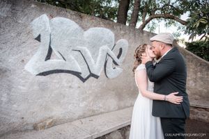 A couple embraces against a textured stone wall in a romantic wedding photo series.