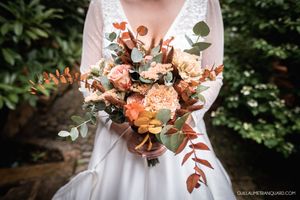 Wedding dress detail with peach and coral floral bouquet against green foliage.