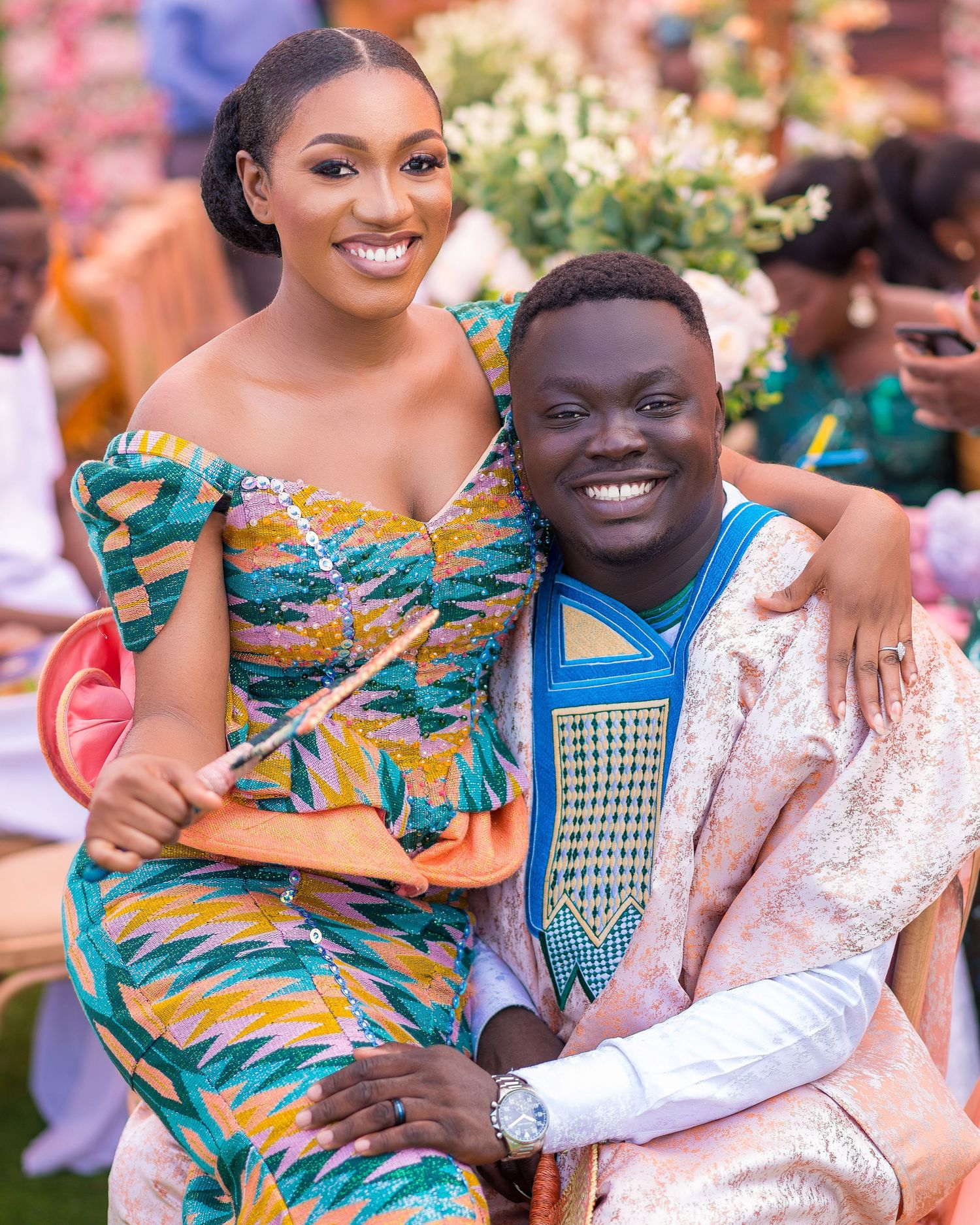 A couple wearing vibrant traditional African prints pose together at a celebration.