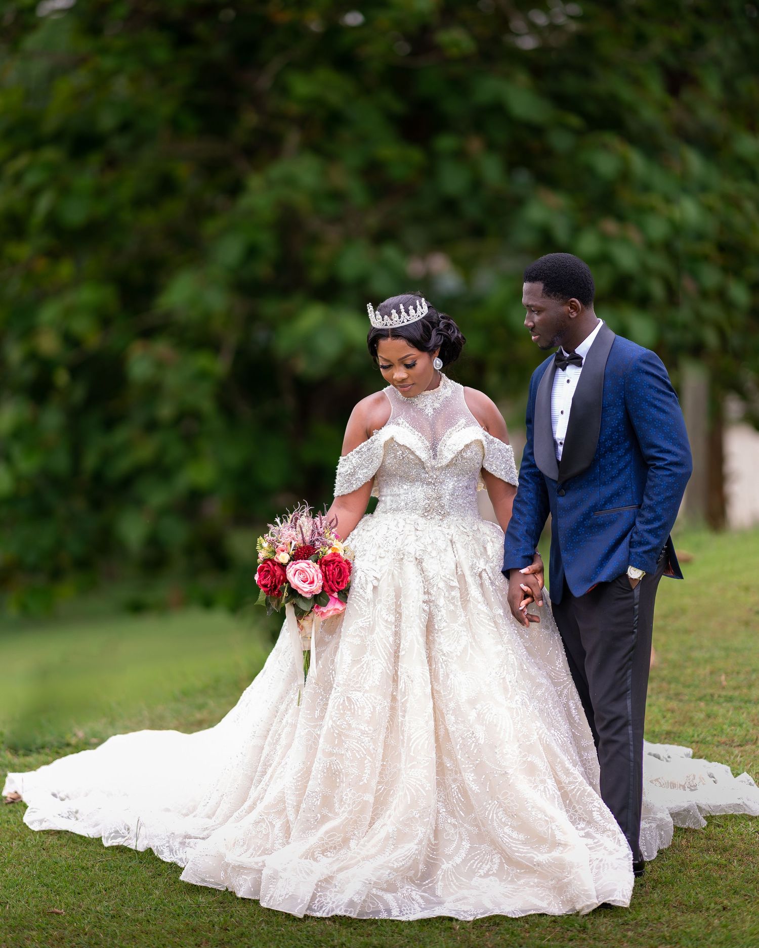 A bride in a flowing white gown poses with her partner on grass during their wedding photoshoot.