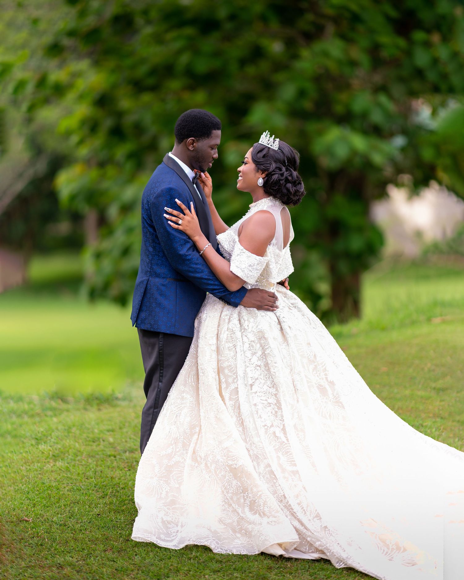 A couple in formal wedding attire shares intimate moments during an outdoor garden photoshoot.