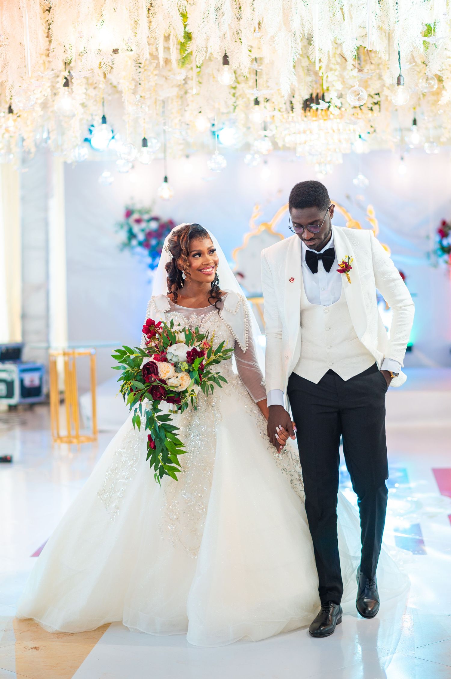 A wedding couple dances together in a bright indoor venue with flowing white dress and formal attire.