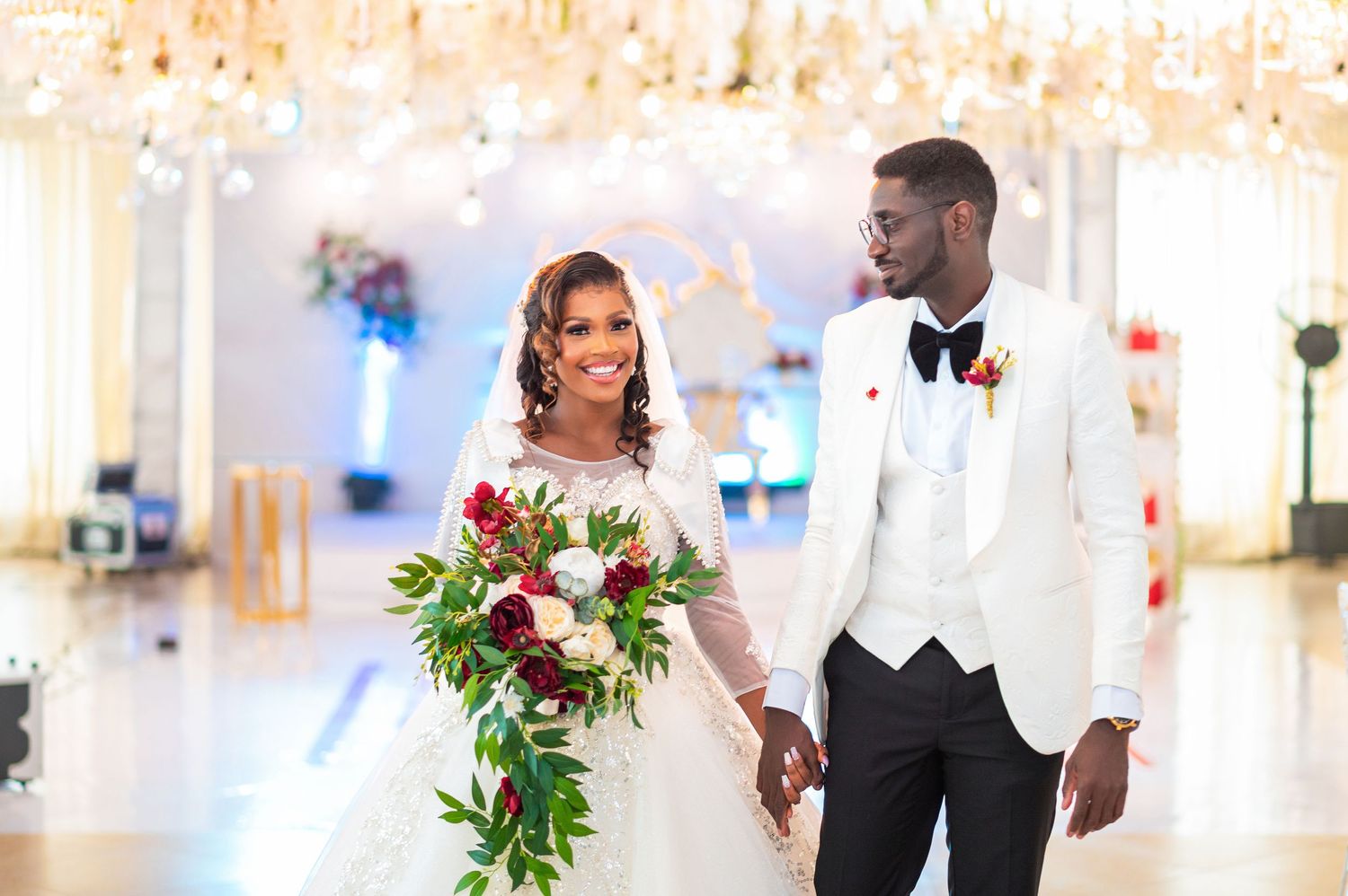 Newlyweds share a romantic moment in an elegant indoor venue with chandelier lighting.