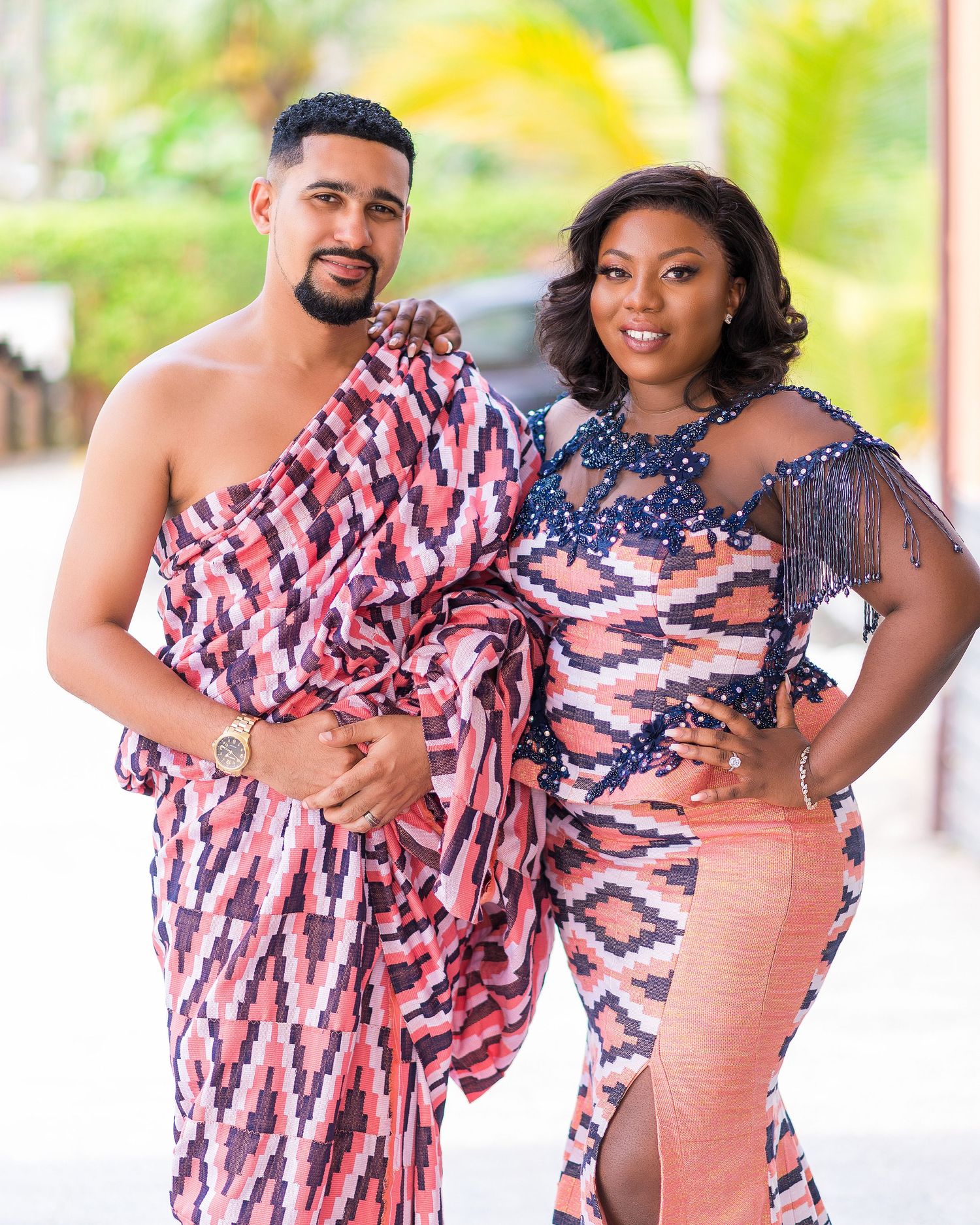 A couple wearing coordinated pink and navy patterned outfits pose together.