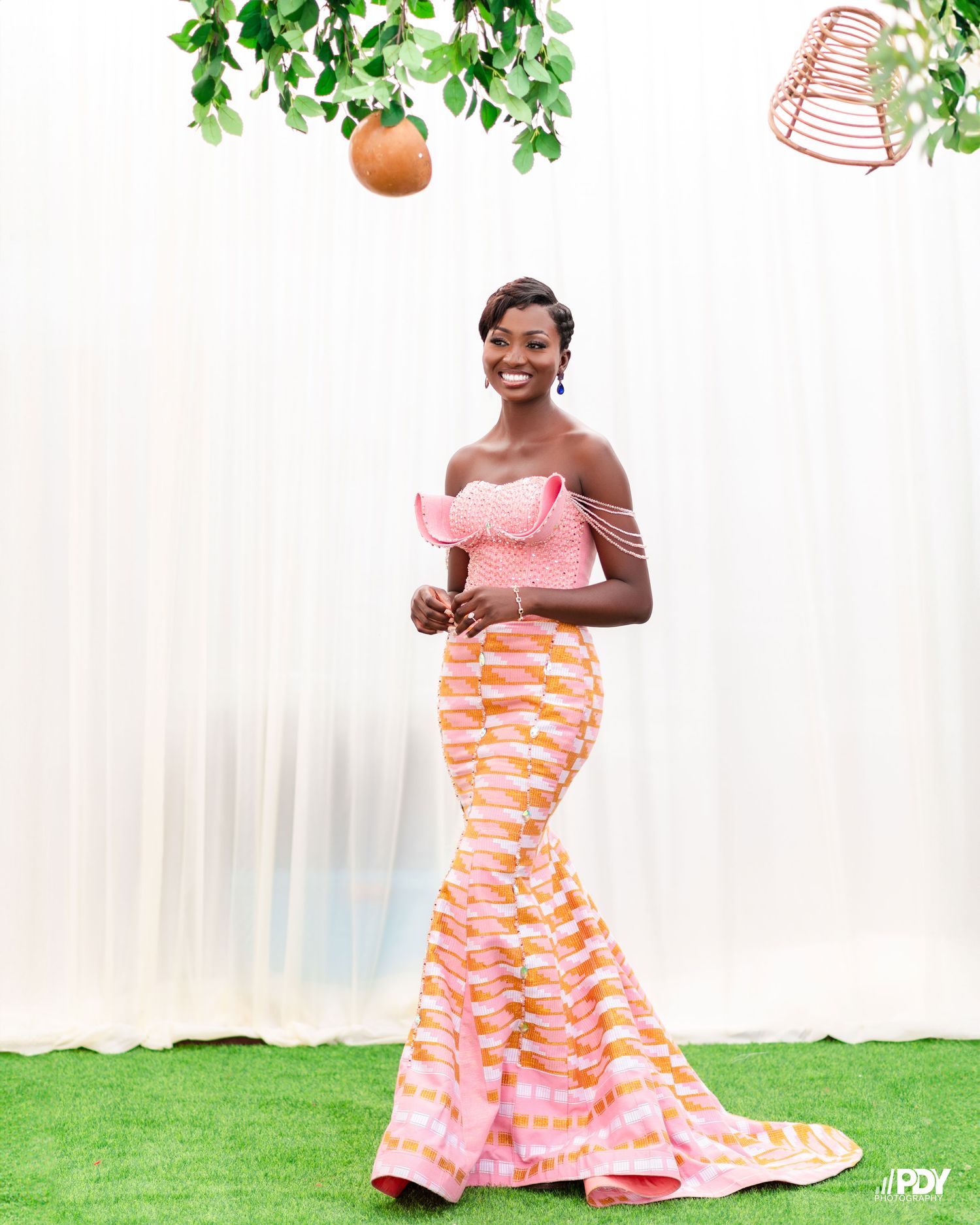 Solo portrait of person in pink off-shoulder top and striped mermaid skirt against white backdrop.