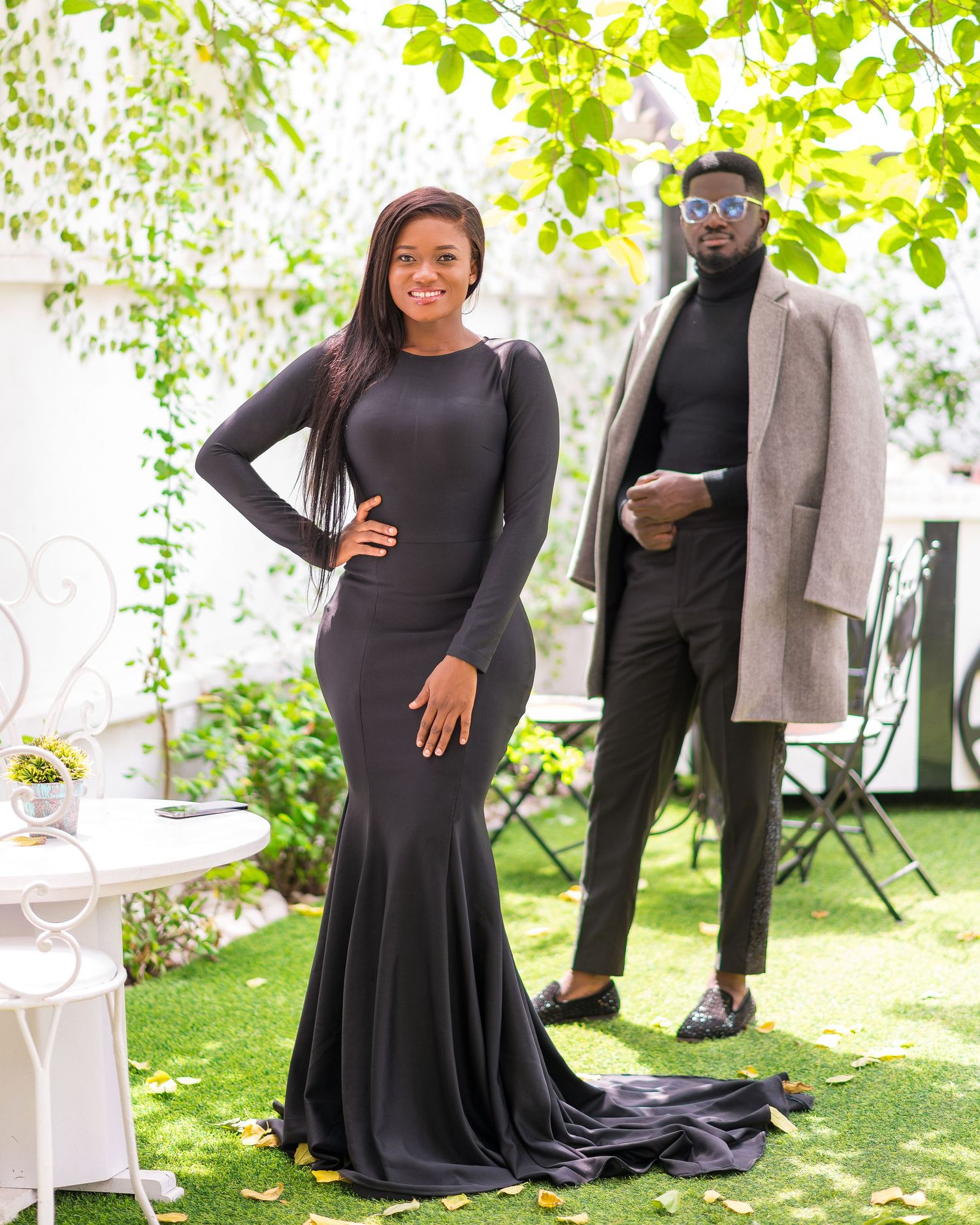 Maternity photoshoot in garden setting with flowing black dress and casual grey outerwear.