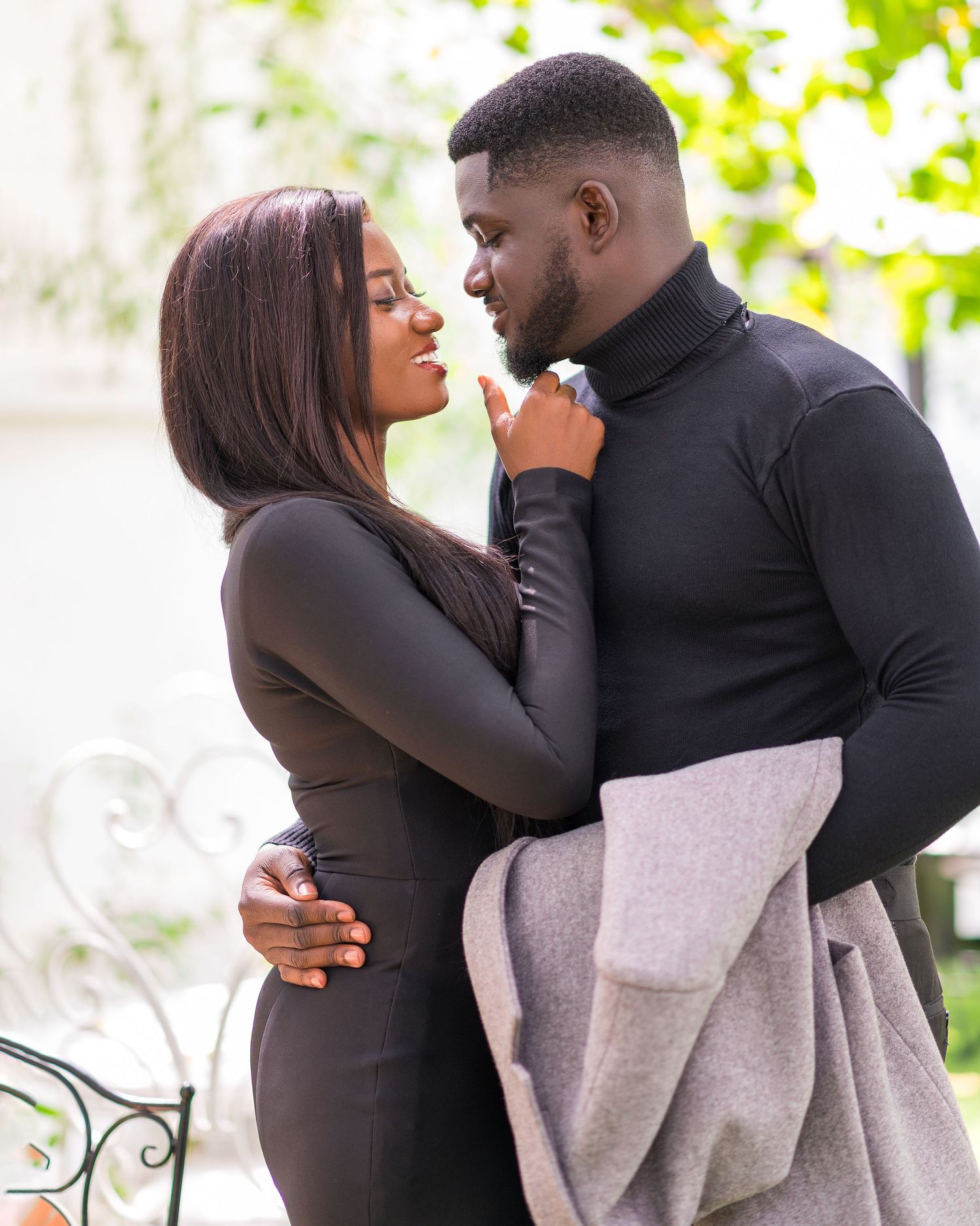 Intimate maternity photo session with couple in black attire and grey wrap against natural backdrop.
