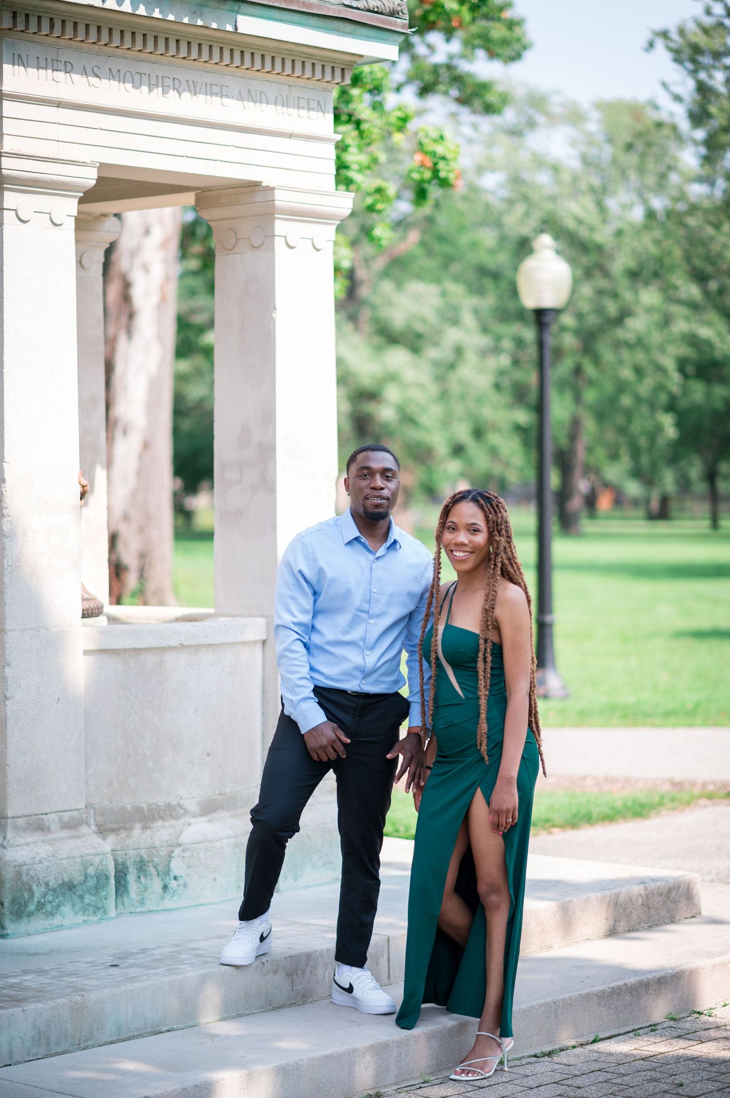 A couple poses on classic stone steps, with her wearing an elegant green dress.