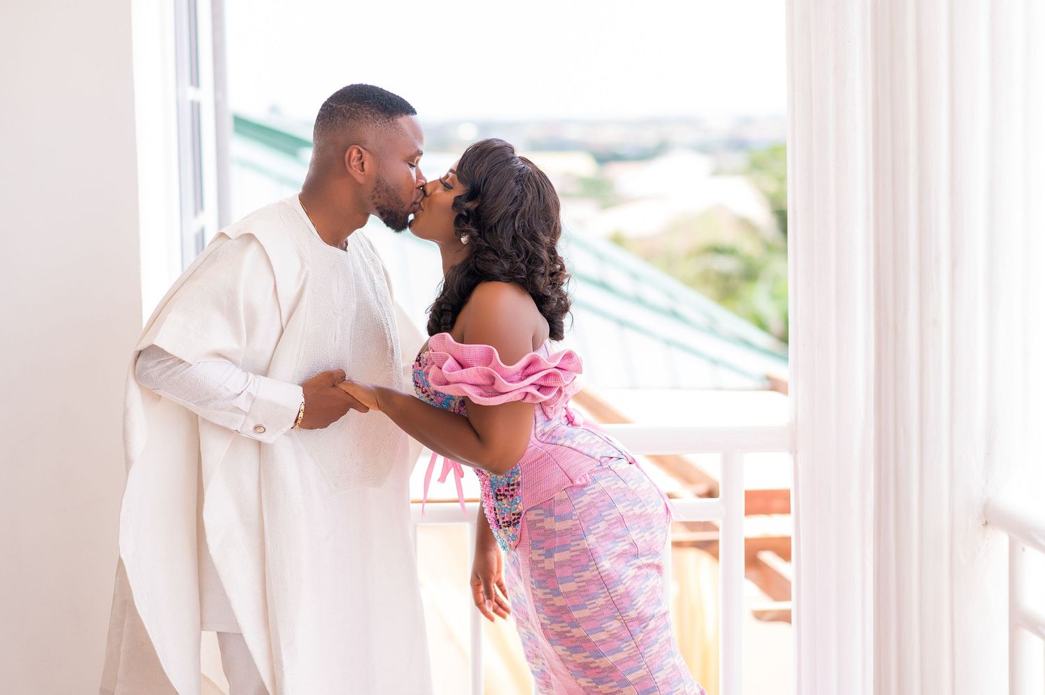 A romantic moment captured between a couple in pink and white attire on a balcony.