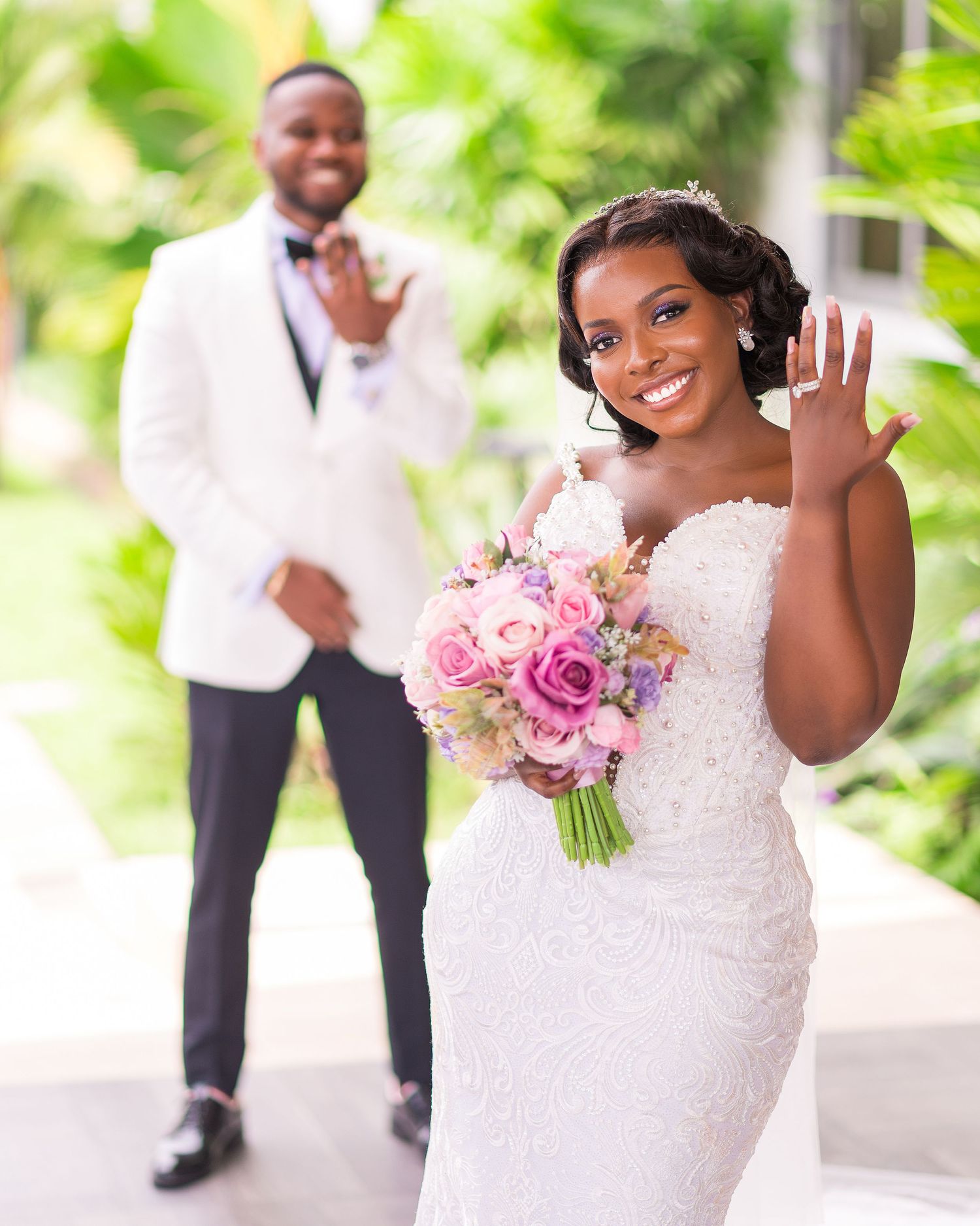 A joyful wedding scene with a bride showing her ring while holding a pink bouquet.