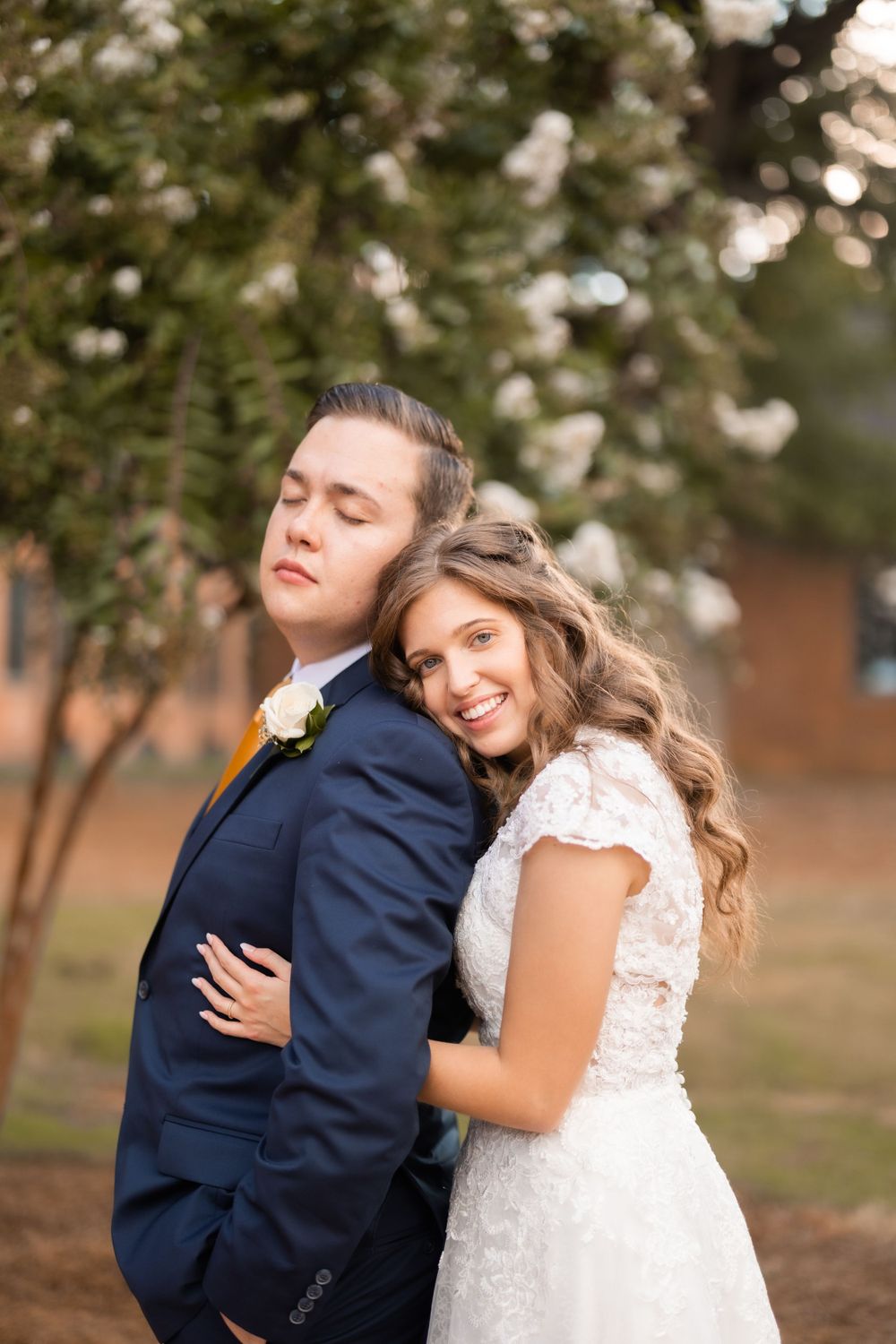 A tender moment between newlyweds in formal attire against a natural backdrop.