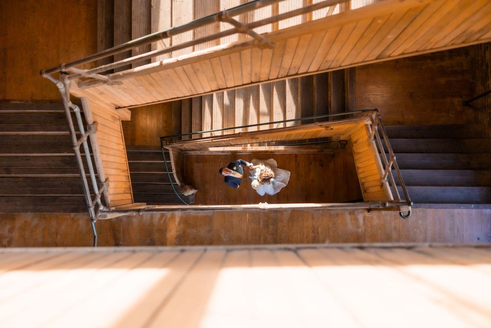 An artistic overhead shot of a wedding dress cascading down a wooden spiral staircase.