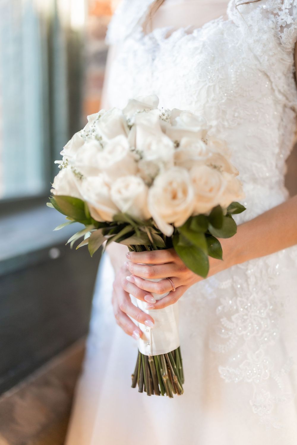 An elegant white rose wedding bouquet held by hands in delicate lace.