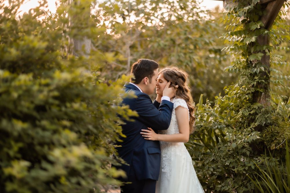 A romantic moment between newlyweds surrounded by lush greenery at sunset.