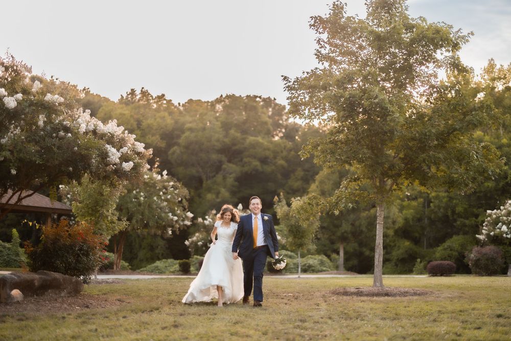 A wedding couple stands in a garden setting during golden hour with trees in the background.