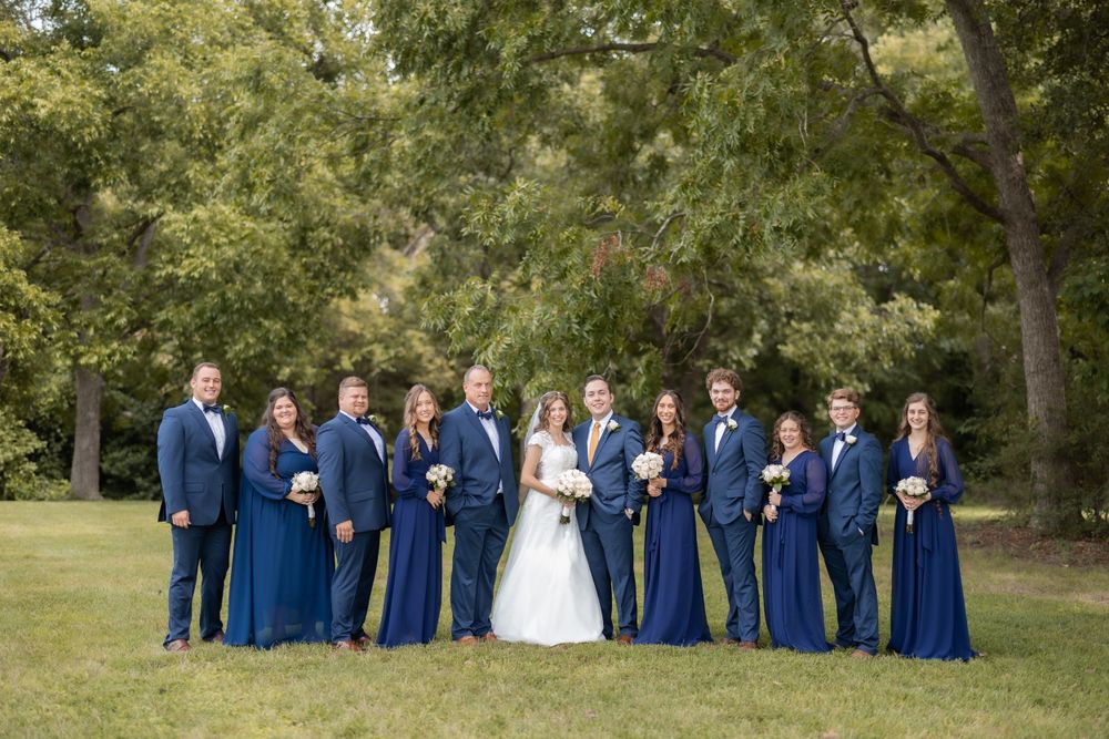 Wedding party in coordinated navy blue attire poses for formal group photo outdoors.