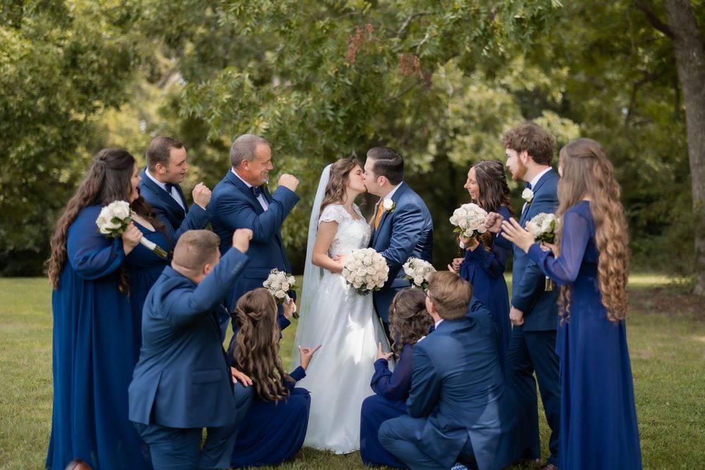 Wedding party in navy attire surrounds couple in celebratory group pose.