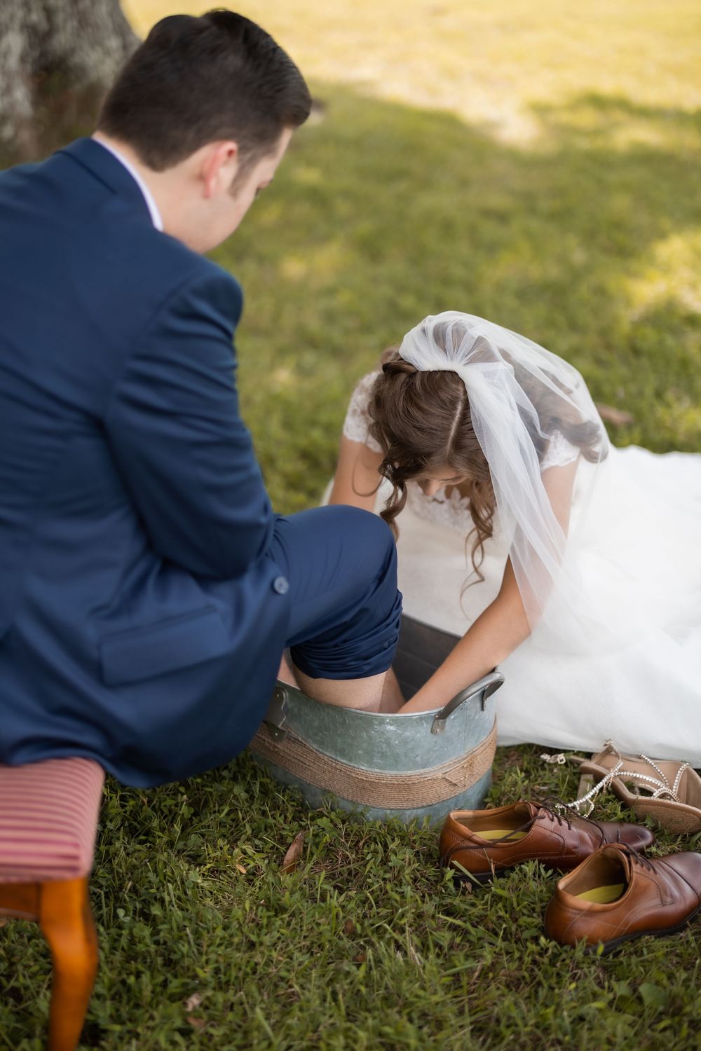 Wedding couple participates in foot washing ceremony with vintage basin outdoors.